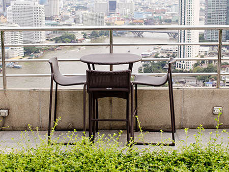 Rattan oone table with two stool chairs standing against the ter
